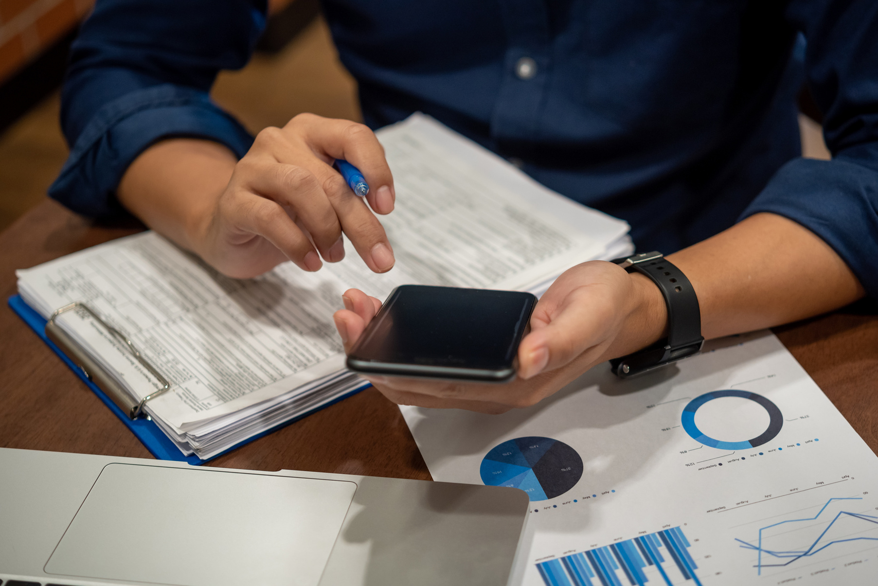 Report charts and graphs marketing financial business analysis and data insights. Hand man holding mobile smartphone on desk.